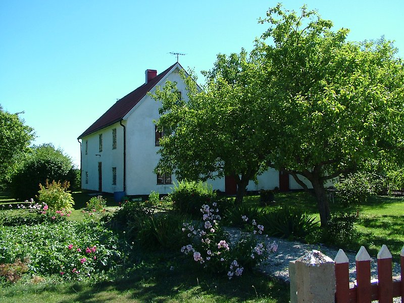 Ett vitt hus med rött tak, en skorsten och en blomträdgård.