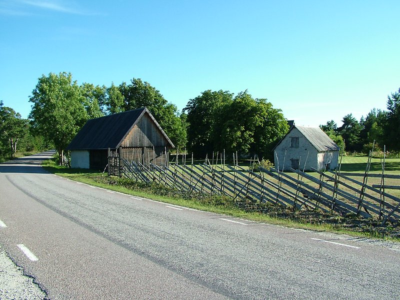 På höger sidan om vägen finns det ett staket och två små byggnader.