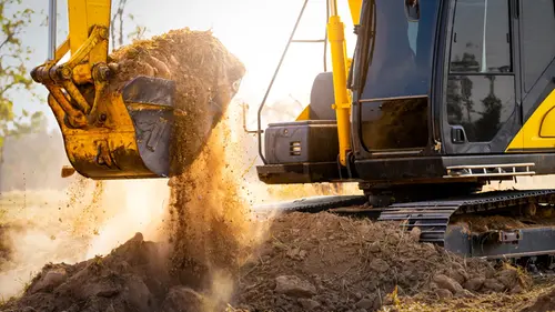 Gul grävmaskin lyfter ett lass jord i skopan