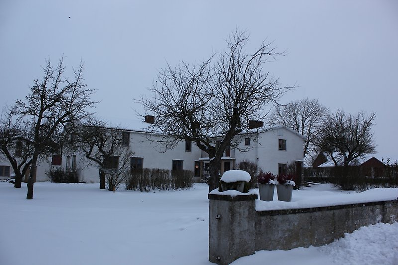 Ett vitt hus bestående av två våningar med gråa fönster och med snö på taket.