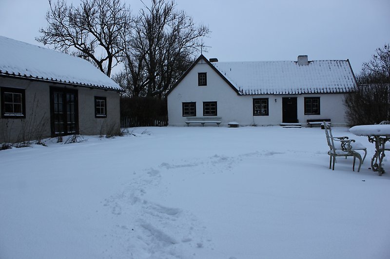Ett vitt hus med svarta fönster, svart ytterdörr och taket är täckt med snön.