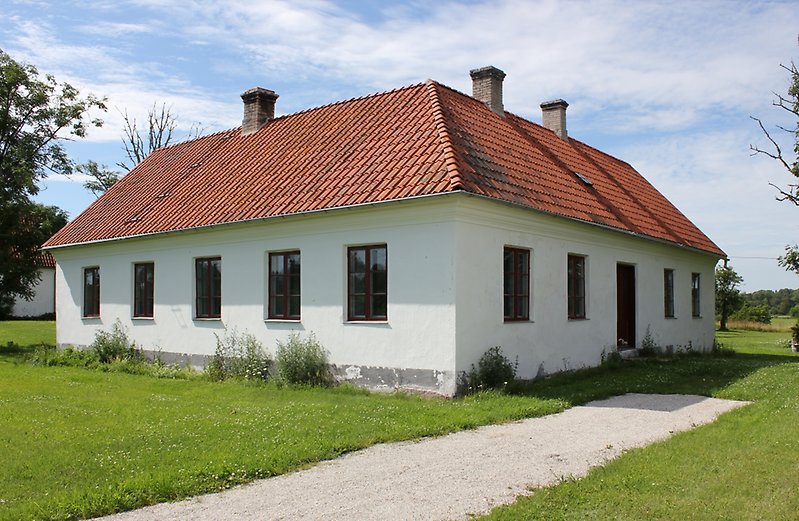 Ett vitt hus med ett rött tak, flera skorstenar, bruna fönster och en brun ytterdörr.