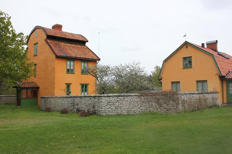 Bakom stenmuren finns det två orangea hus med gröna fönster och röda tak.