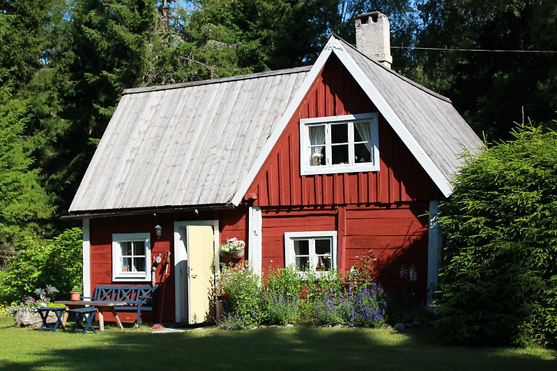 En sagolik röd stuga med trätak, vita fönster och en skorsten.