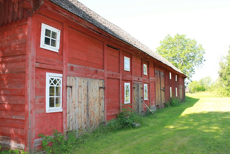 En röd lada med portar av obehandlat trä, vita fönster och ett rött tak.