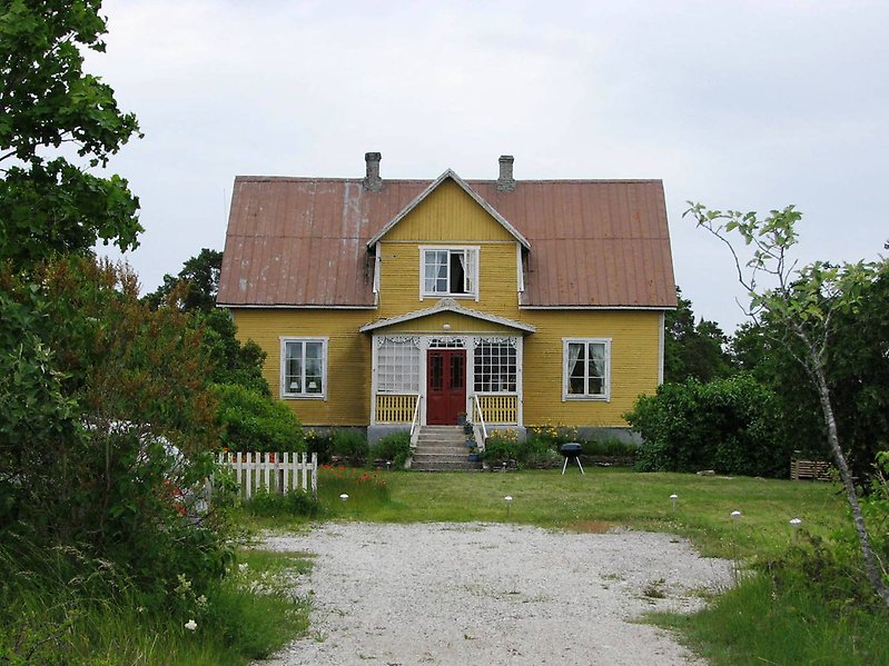 Ett tvåvånings hus med gul fasad, vita fönster och ett brunt plåttak med två skorstenar.