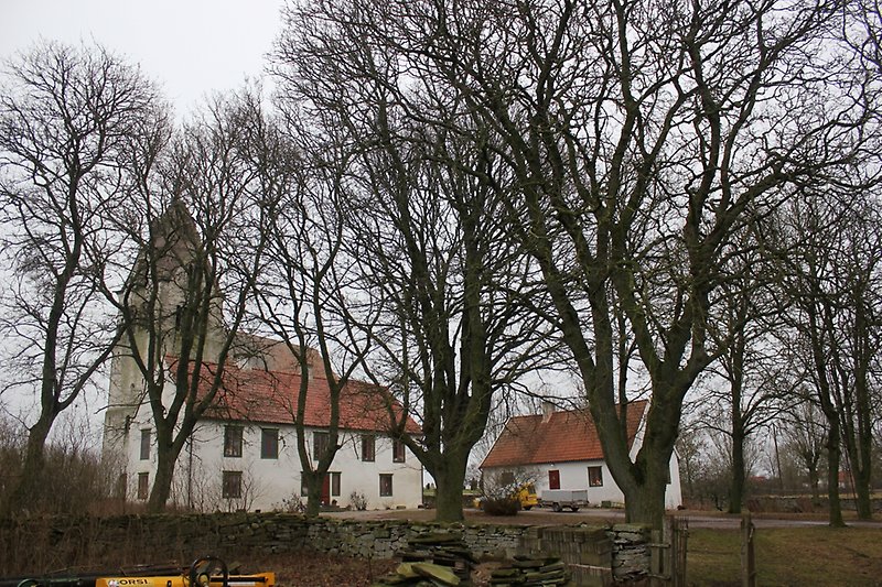 På kyrkans baksida finns två vita byggnader med röda dörrar och tak.