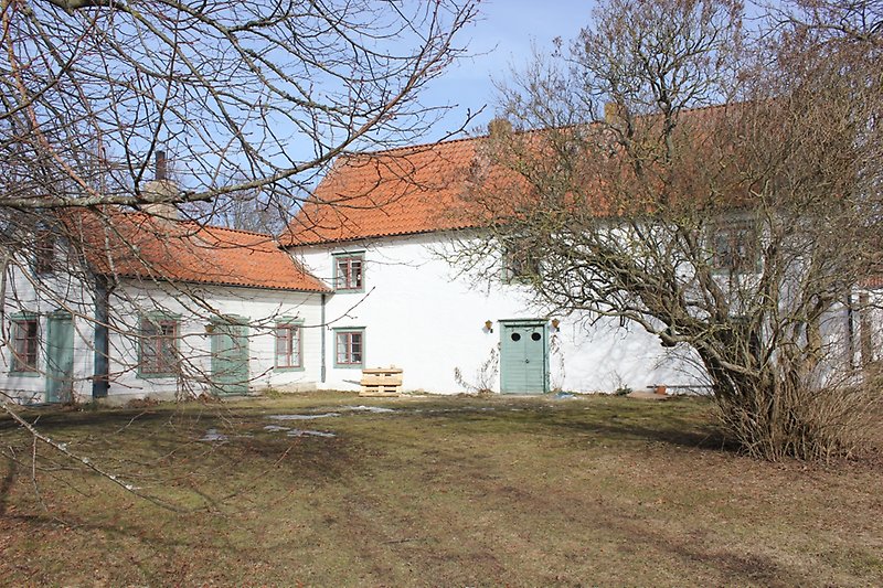 Ett vitt hus med bruna fönster, gröna fönsterramar, gröna dörrar och ett rött tak.