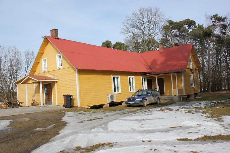 Ett gult hus med träfasad, vita fönster, ett rött plåttak och två skorstenar.
