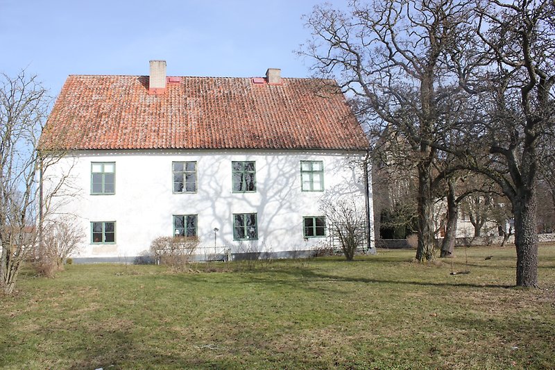 Ett vitt hus med gröna fönster och ett rött tegeltak med två skorstenar.