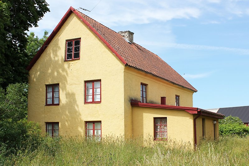 Ett gult hus med röda fönster och ett rött tak med en skorsten.