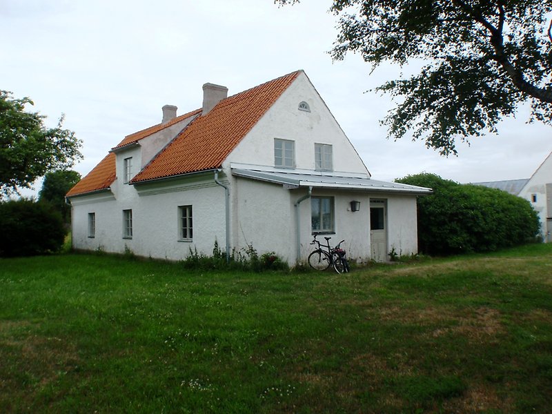 Ett vitt hus med rött tak, två skorstenar och en parkerad cykel på gården.