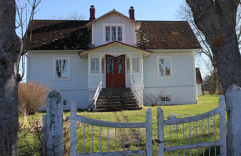 Ett vitt hus med en träfasad, vita fönster och en röd ytterdörr.
