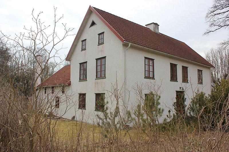Ett vitt hus av två våningar, bruna fönster, gröna fönsterramar och ett rött tak.