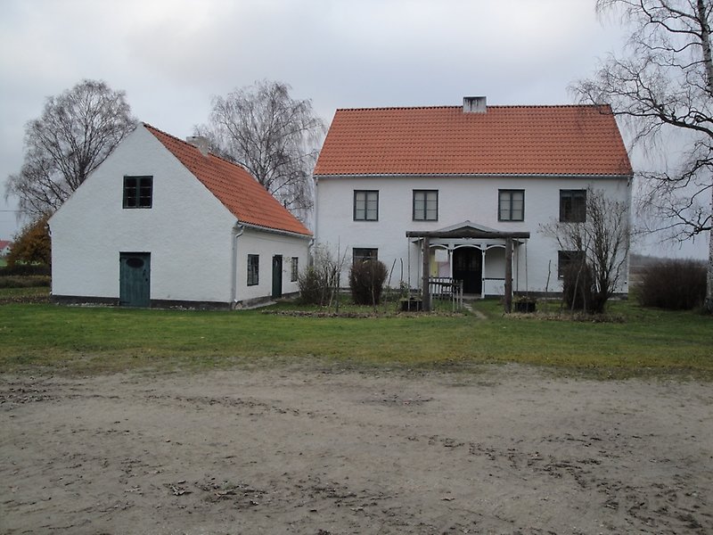 Två vita hus med gröna dörrar, gröna fönster och röda tegeltak.