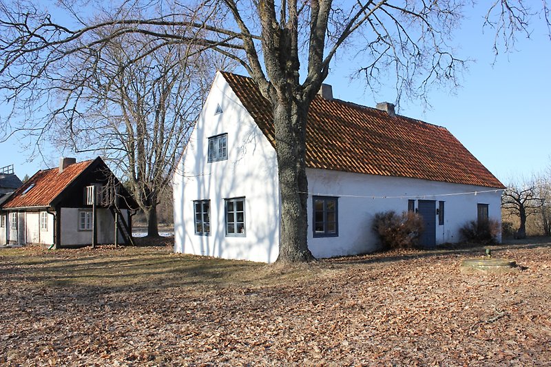 Ett vitt hus med gråa fönster, en grå ytterdörr och ett rött tegeltak med två skorstenar.