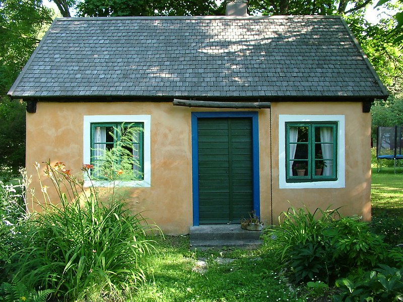 En nyrenoverad liten stuga med gula väggar, gröna fönster och en grön ytterdörr med blåa detaljer.