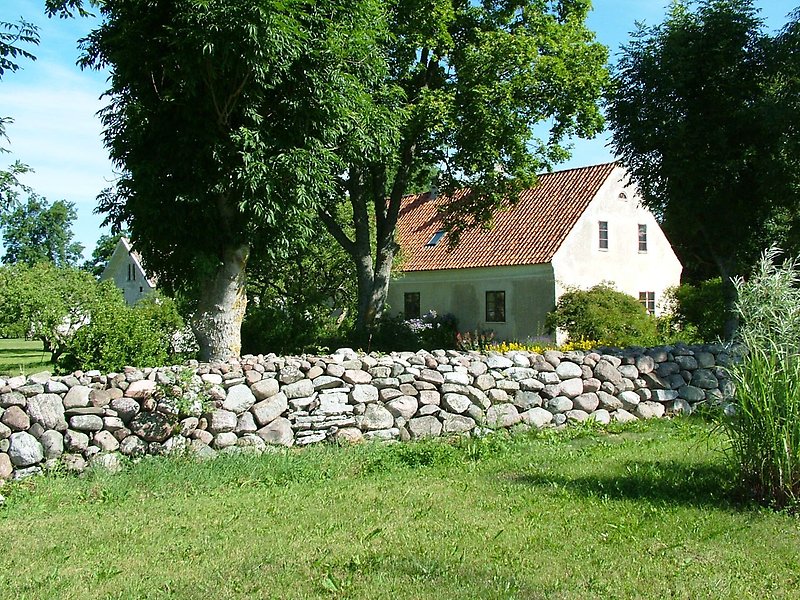Ett vitt hus, grön gräsmatta och en mur av natursten.
