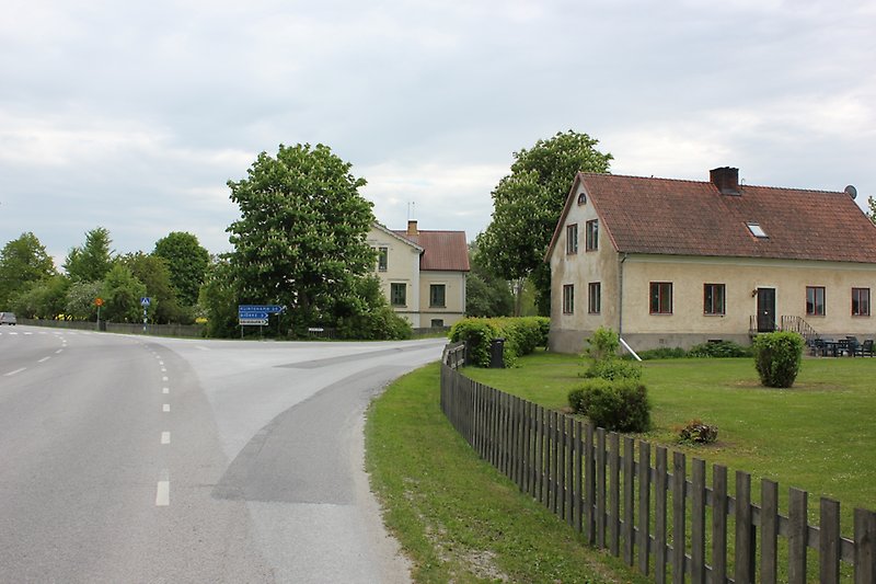 På höger sida av bilvägen finns det ett gult hus med bruna fönster och ett orange tak.