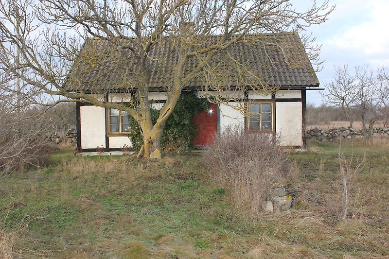 Ett vitt litet hus med svarta trädetaljer, bruna fönster och en röd ytterdörr.