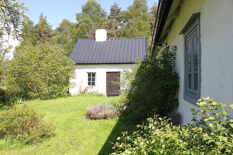 På gården finns ett vitt hus med blåa fönster och ett svart plåttak. Det finns även en vit stuga som också har ett svart plåttak.
