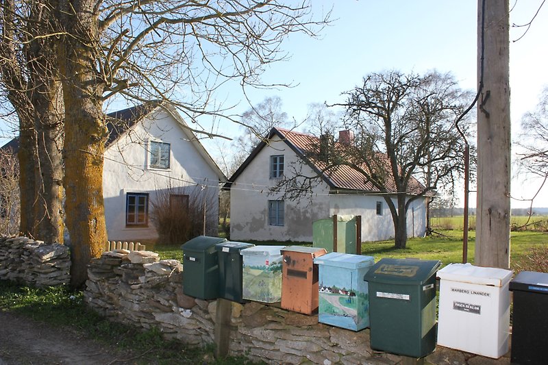 Flera postboxar finns längs vägen. Längre bak, bakom en stenmur, finns även två vita hus med blåa fönster och röda tak.