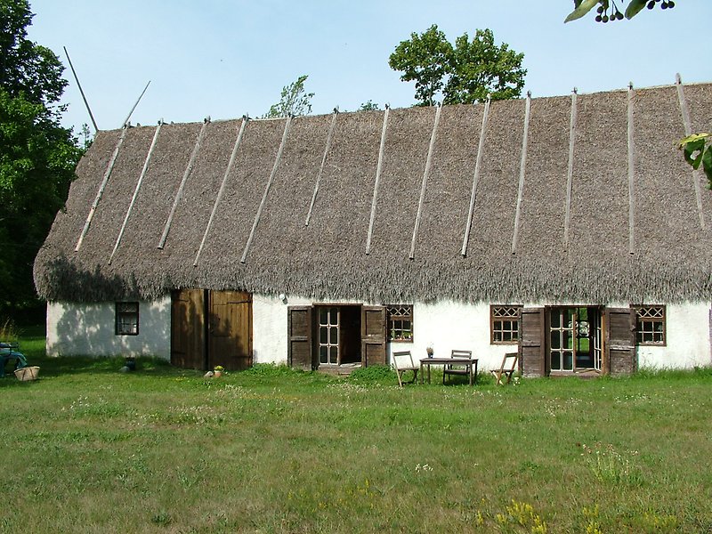 Ett gammalt vitt stenhus med träfönster, trädörrar och ett agtak.