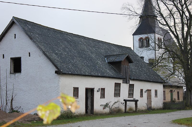 En vit ladugård med ett svart tak och en vit kyrka.