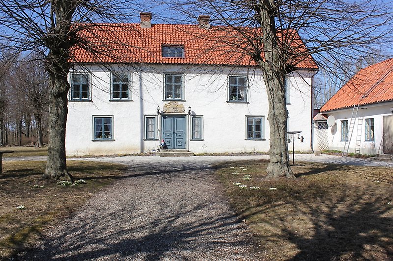 Ett vitt tvåvåningshus med gråa dörrar, gråa fönster och ett rött tegeltak med två skorstenar.