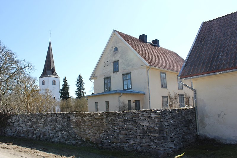 Bakom stenmuren står det ett gult hus och längre bort syns Fardhems kyrka.