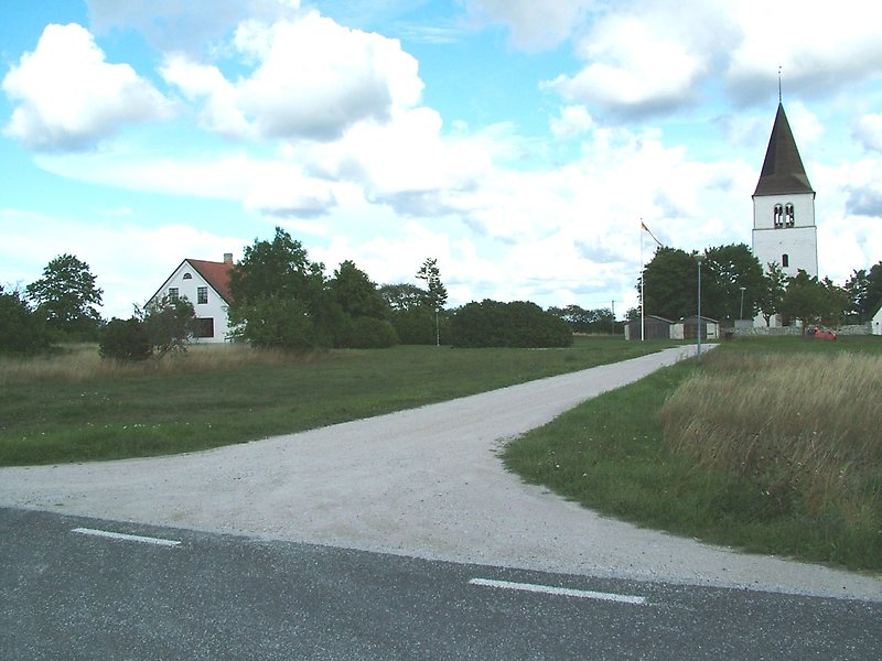 På slutet av grusvägen finns en vit kyrka med ett svart tak.