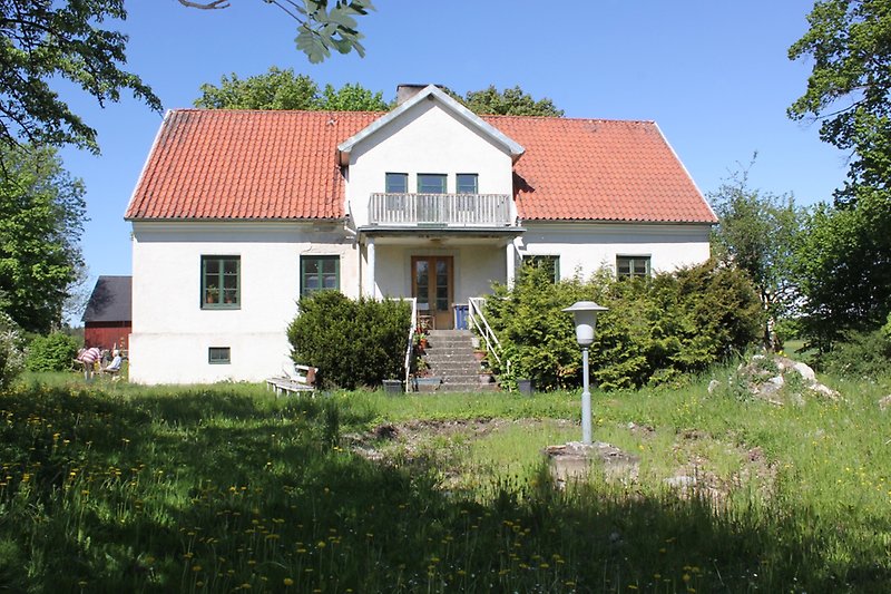 Ett vitt hus gröna fönster, en brun ytterdörr och ett rött tegeltak.