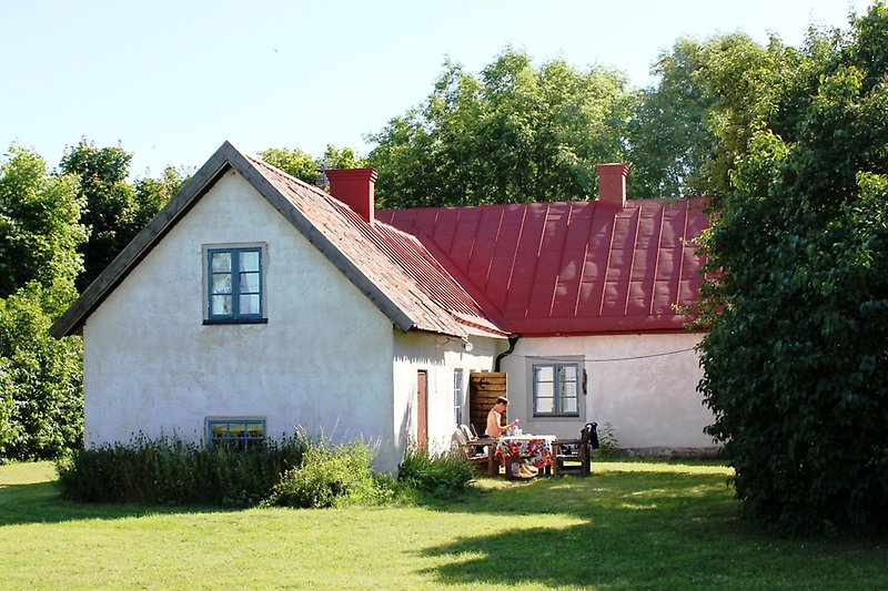 Ett vitt hus med bruna trädörrar, blåa fönster och ett rött plåttak.
