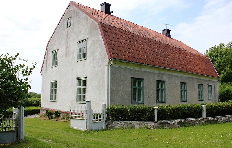 Ett vitt tvåvåningshus med olivgröna fönster och ett rött tegeltak med två skorstenar.