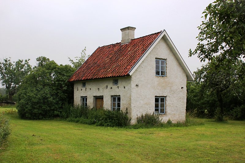 Ett vitt litet hus med blåa fönster och ett rött tegeltak med en skorsten.