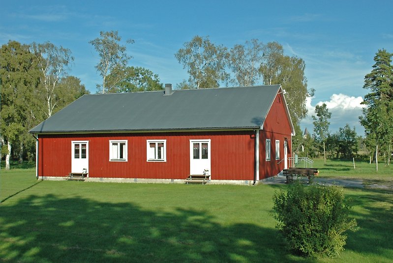 En röd träbyggnad med vita dörrar, vita fönster och ett svaret plåttak.