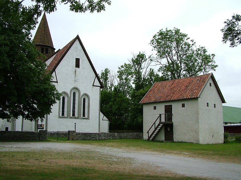 En vit kyrka och en liten stuga med ett rött tegeltak.