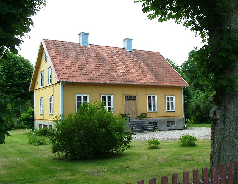 En gul byggnad med bruna dörrar, vita fönster och ett rött tak med två skorstenar.